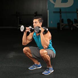 a man squats with two dumbbells in front of his face as he holds a barbell