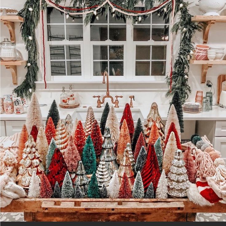 a table topped with lots of christmas trees next to a kitchen counter covered in holiday decorations