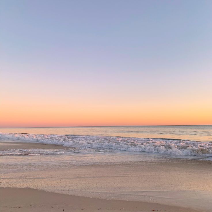 an ocean beach with waves coming in to shore and the sun setting on the horizon