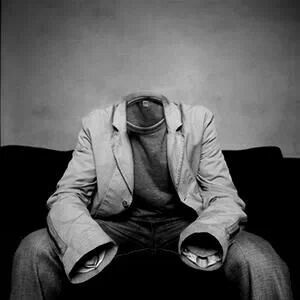 a man sitting on top of a black couch in front of a wall with a coat over his head