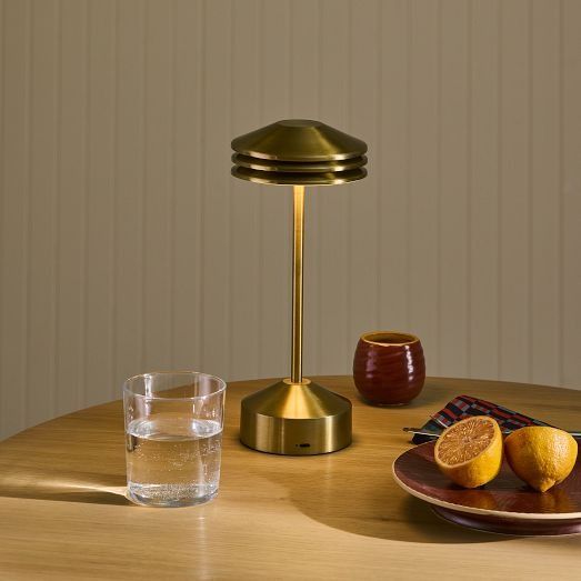 a table topped with a plate of fruit next to a lamp and a glass filled with water