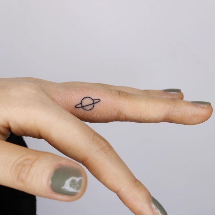 a woman's hand with a small saturn tattoo on it, and the word saturn written in black ink