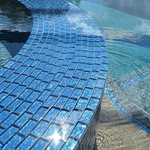 a pool with blue glass tiles on the edge and water reflecting off it's surface