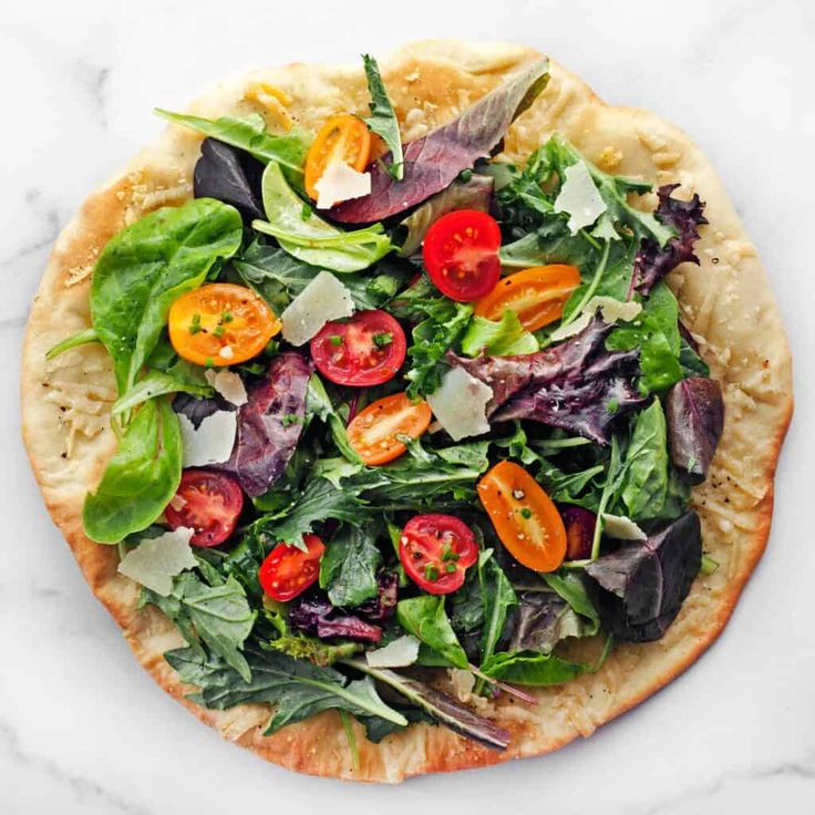 a pizza topped with lots of veggies on top of a white counter