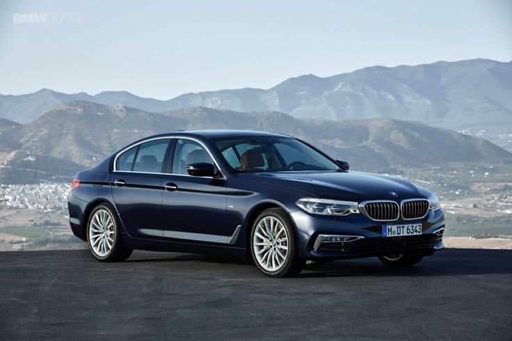 a blue bmw car parked in front of mountains and cityscape on a sunny day