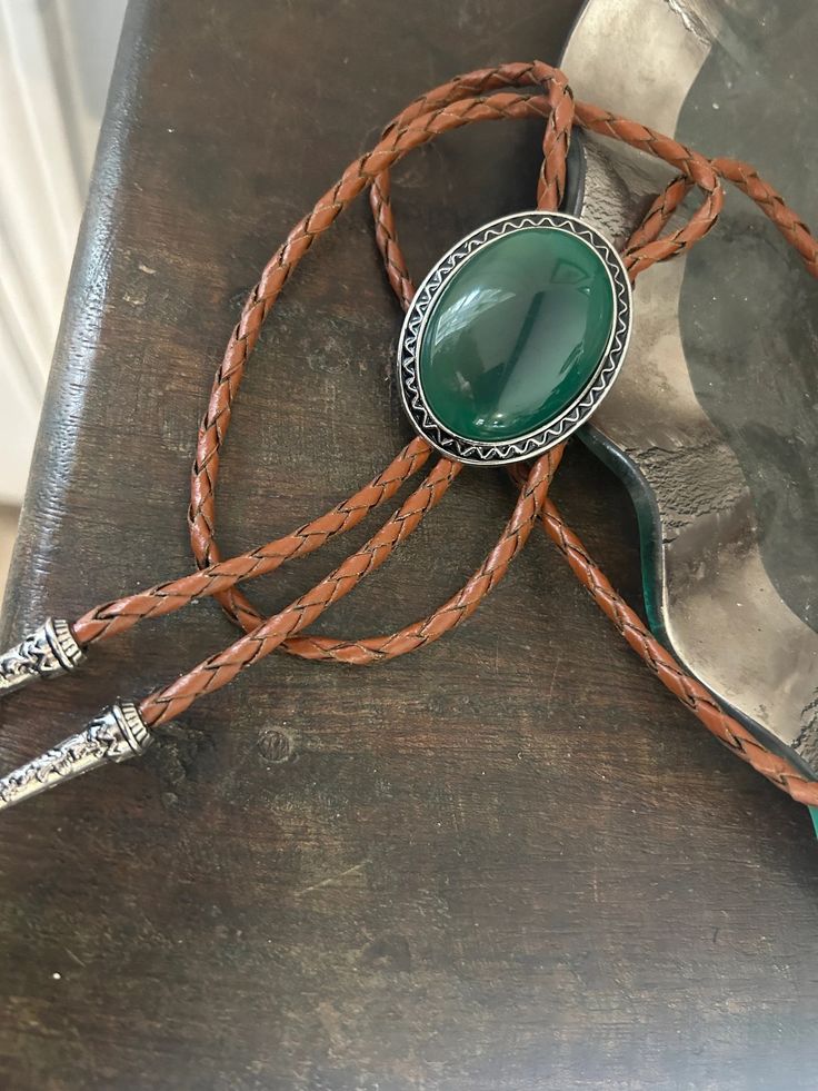 This awesome bolo tie has a southwestern design and green agate centerpiece. The cord is genuine leather. All the stones will vary slightly. Our bolos pair nicely with many of our belt buckles! They make wonderful gifts. The western bolo tie rope length is 39'' ; charm agate stone pendant size is 2'' x 1 1 /2'' Bohemian Bolo Ties For Western-themed Events, Western Style Necklace With Adjustable Cord, Bohemian Lariat Bolo Tie For Rodeo, Bohemian Bolo Tie For Rodeo, Rustic Green Adjustable Jewelry, Western Lariat Bolo Tie With Adjustable Length, Western Bolo Ties With Adjustable Length, Western Style Lariat Bolo Tie With Adjustable Length, Adjustable Concho Lariat Jewelry