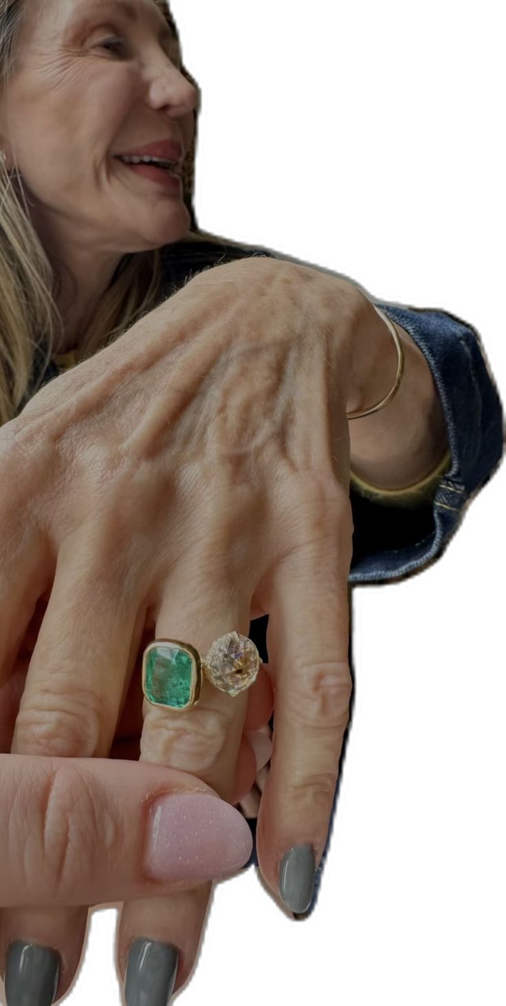 a woman holding onto her hand with an emerald and diamond ring on it's finger