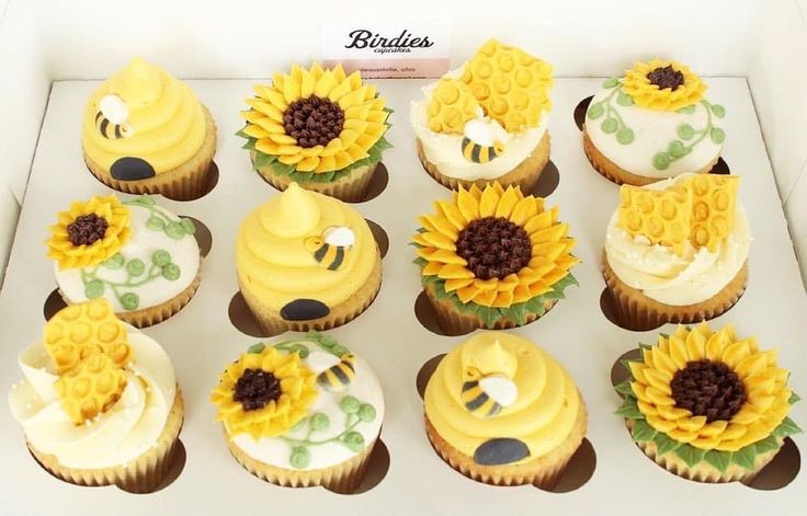 cupcakes decorated with sunflowers and bees are on display in a box