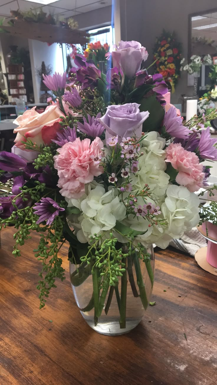 a glass vase filled with lots of flowers on top of a wooden table in a room