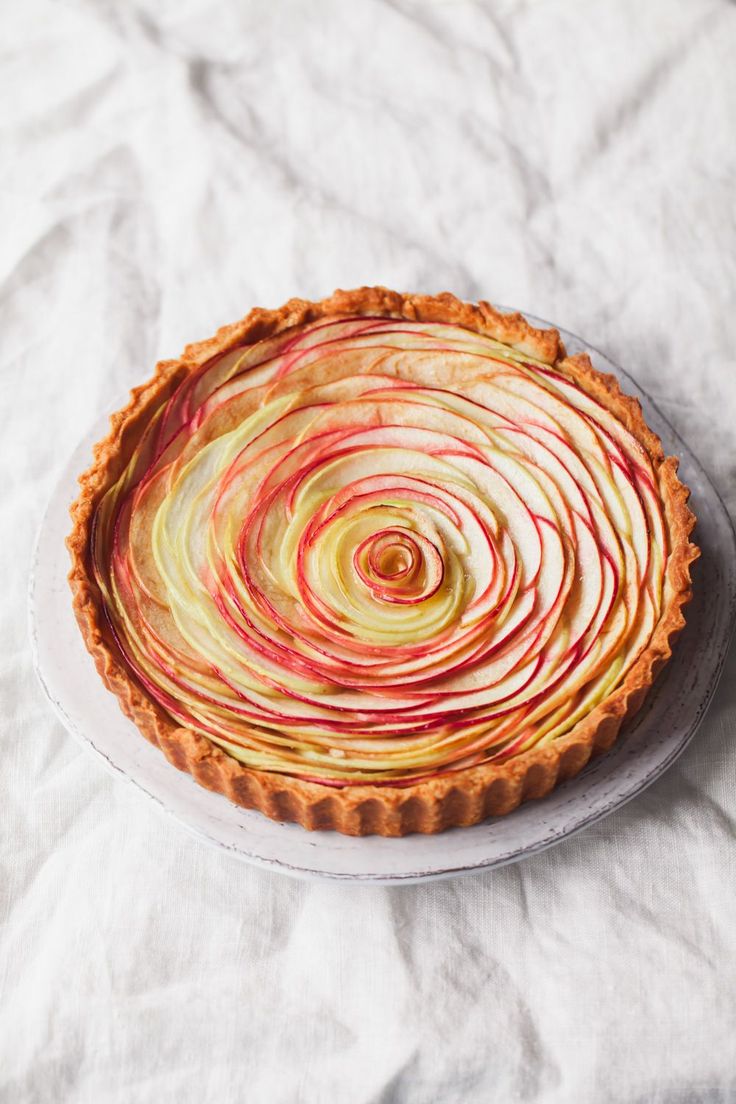 an apple pie on a white plate with red and yellow swirls in the crust