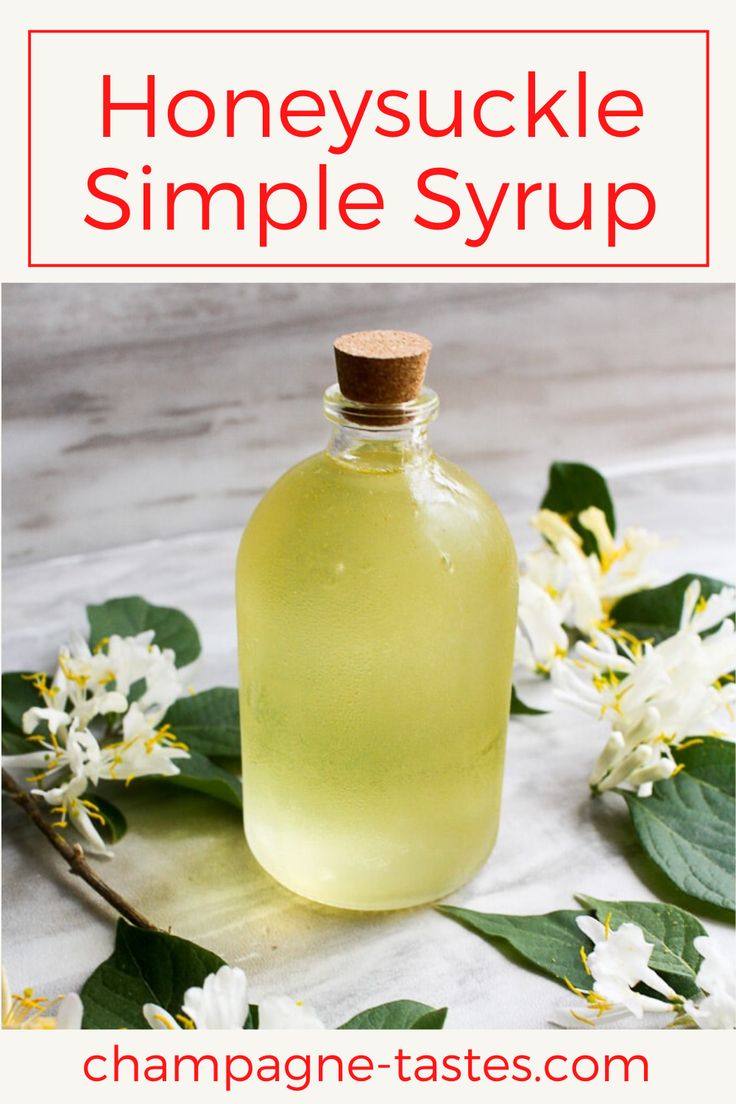 a bottle of honeysuckle simple syrup sitting on a table with flowers and leaves