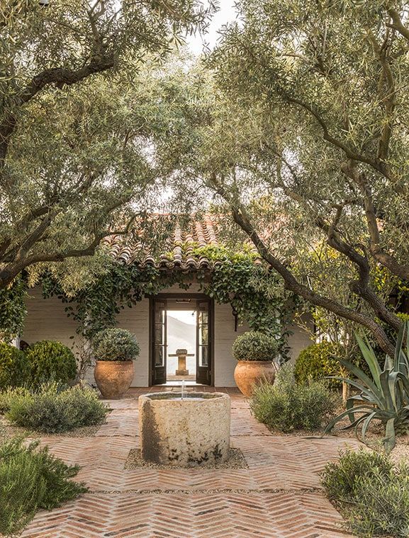 an outdoor courtyard with trees, plants and a water fountain in the center surrounded by brick pavers