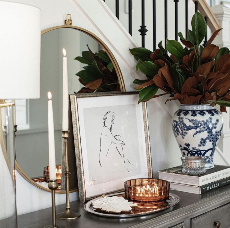 a table topped with a vase filled with flowers next to a mirror and two candles