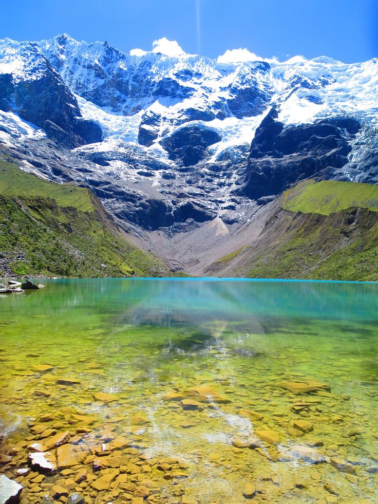 the mountains are covered in snow and green water, with rocks on the ground below