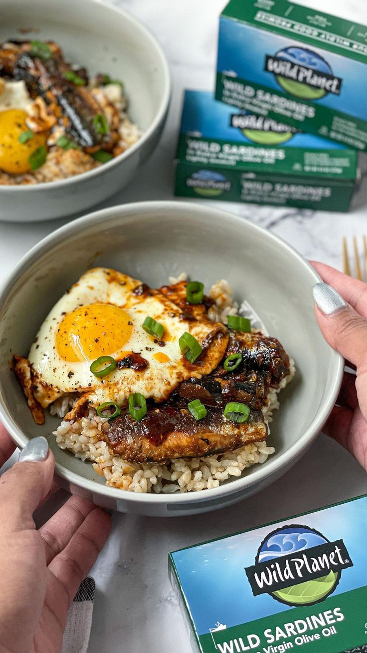 someone holding a bowl of food with rice and an egg on it next to two packets of wild planet