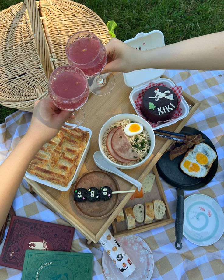 two people are toasting with wine and food on a picnic blanket