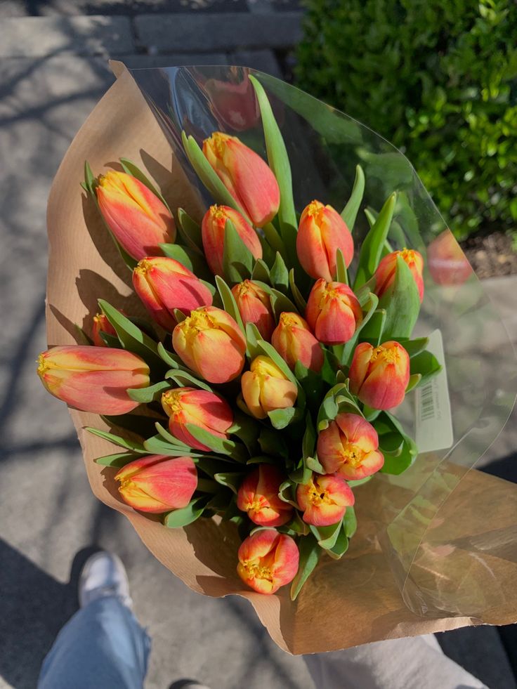 a bouquet of tulips is held by someone's hand on the sidewalk