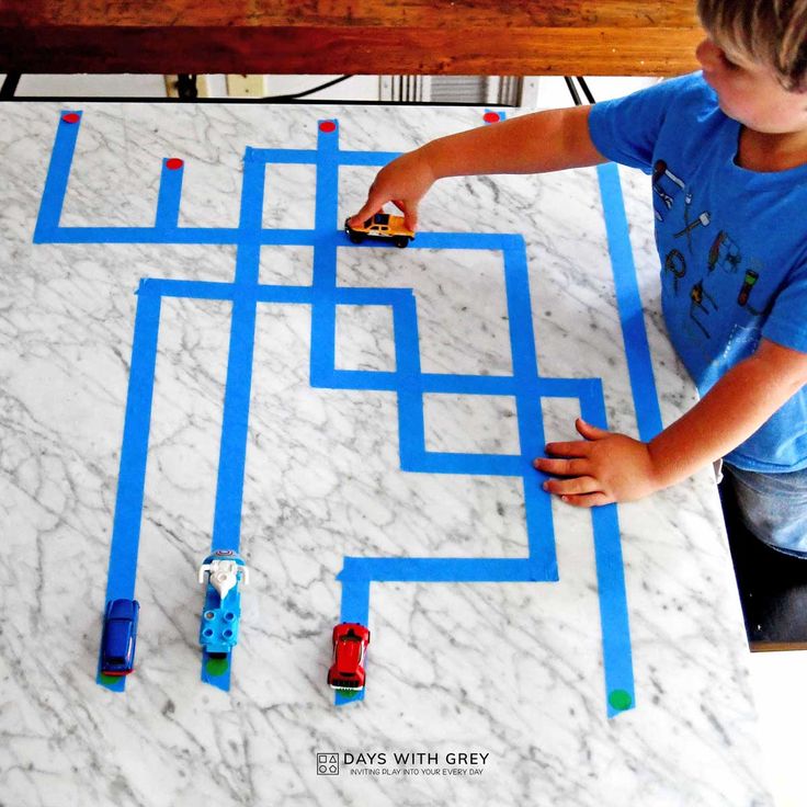 a young boy is making a maze with legos on the marble counter top and blue tape