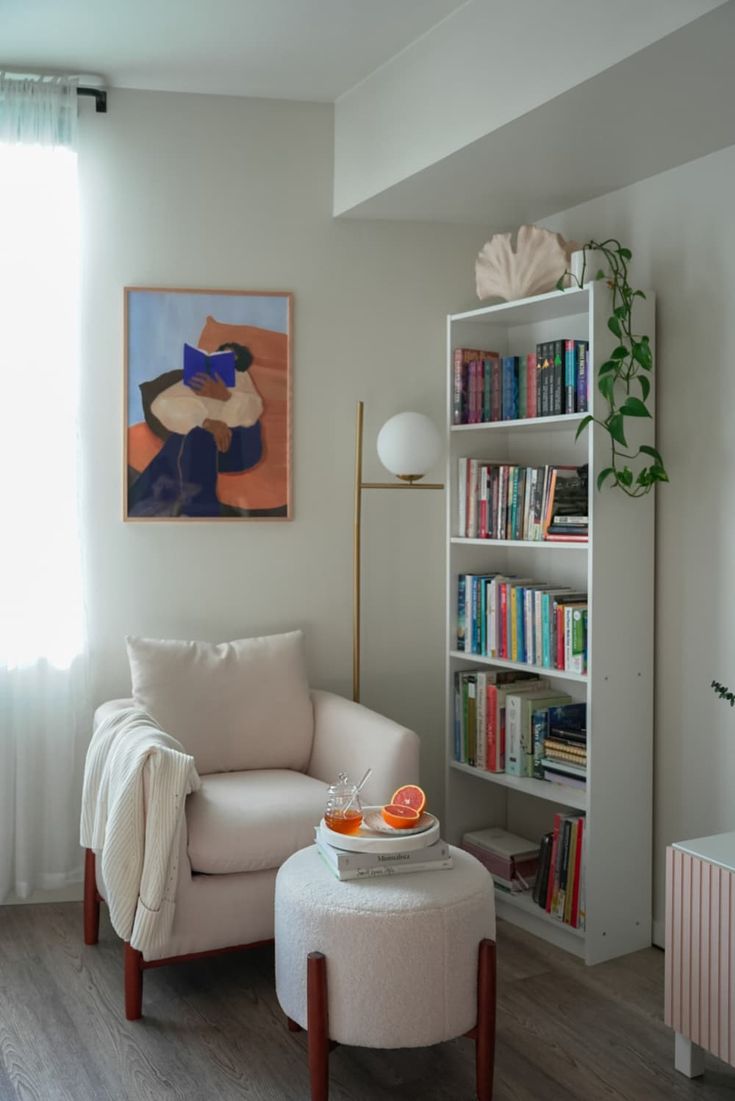 a white chair and ottoman in a room with bookshelves, windows, and a painting on the wall