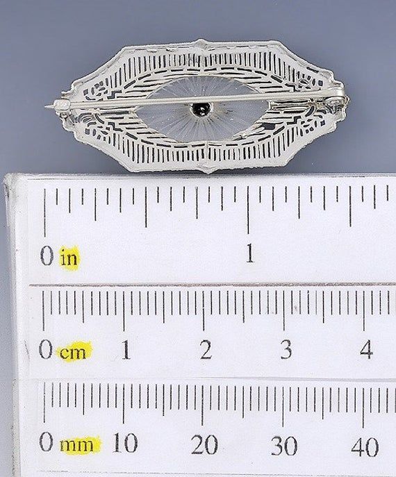 Presented is an elegant 14 karat white gold, crystal and diamond brooch or pin. This piece dates to around the 1910s-1920s and is likely of American make. The pin is done in a beautiful delicate filigree design, set with an oval of clear crystal. This crystal has a carved rayed design, surrounding a single diamond. This piece is in great overall condition. The clasp functions well and closes securely. There is a small break to the filigree, visible at about the 8 'clock position beside the cryst Diamond Brooch, Filigree Design, Diamond Crystal, Clear Crystal, Brooch Pin, White Gold, Carving, Crystals