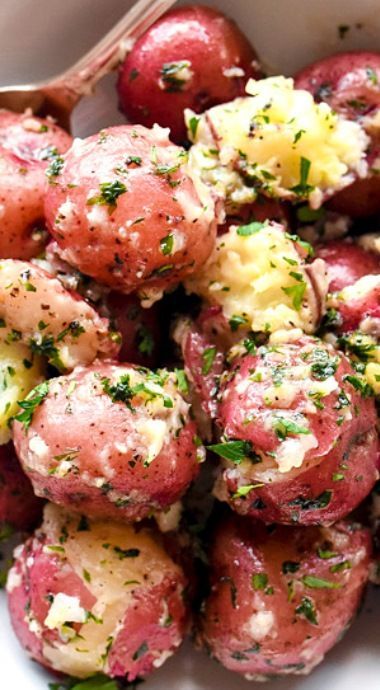 a white bowl filled with red potatoes covered in cheese and herbs