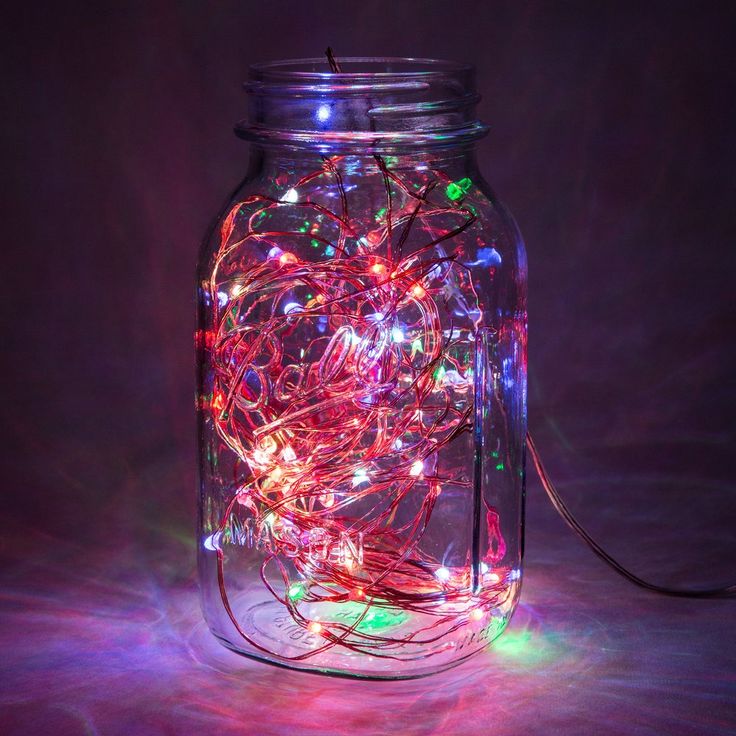 a glass jar filled with lots of lights on top of a table next to a cord