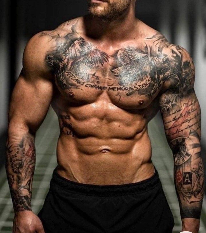 a shirtless man with tattoos on his chest standing in a hallway and looking at the camera