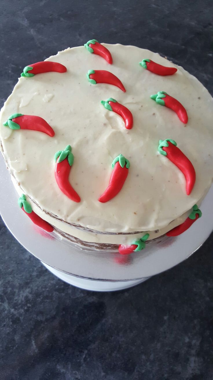 a cake with white frosting and red chili peppers on the top is sitting on a plate