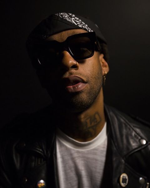 a man wearing sunglasses and a hat with tattoos on his head is looking at the camera