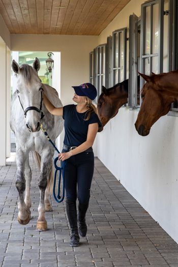 a woman leading two horses down a hallway