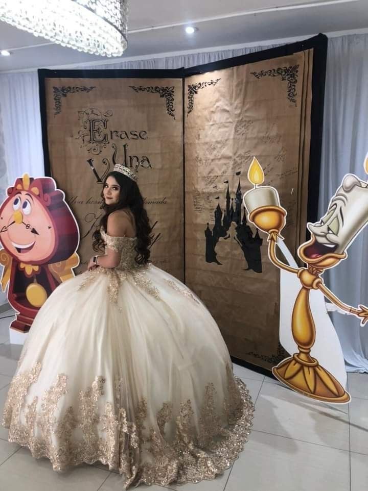 a woman in a white and gold dress standing next to a wall with beauty and the beast images on it