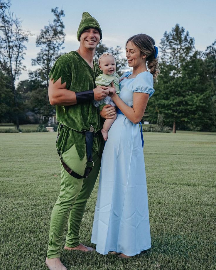 a man and woman dressed as peter panton with a baby in his lap, standing on the grass