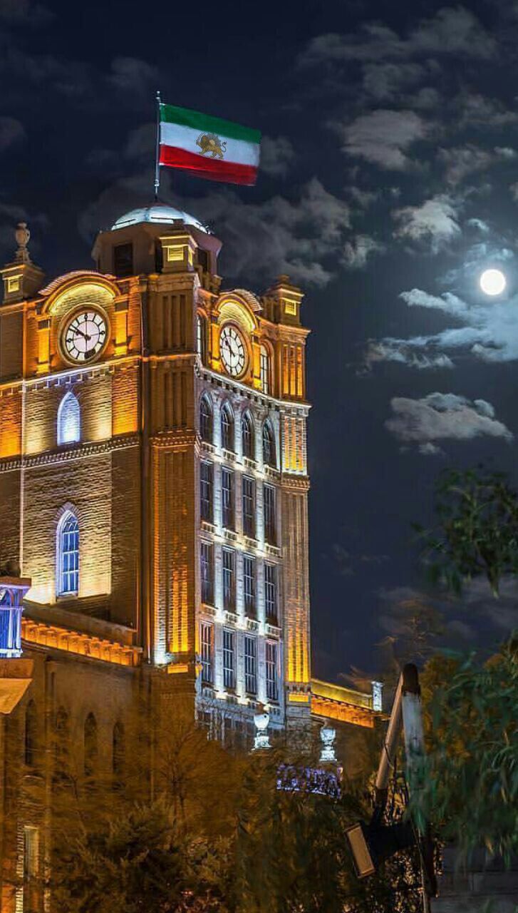 a large clock tower lit up at night with the moon in the sky behind it