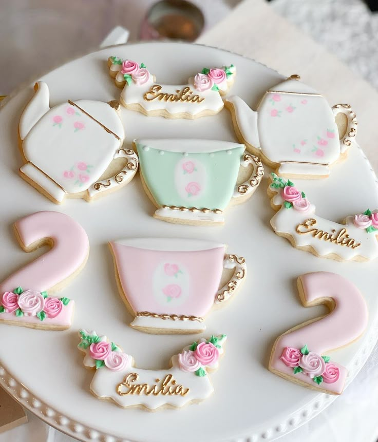 decorated cookies are arranged on a white cake platter with pink and green accents, along with baby's first names