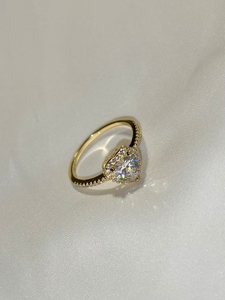 Introducing our Classic Sparkling Heart Ring, a breathtaking piece that exudes elegance and sophistication. Crafted from luxurious gold, this exquisite ring features a stunning large, round central gemstone, reminiscent of a dazzling diamond, encircled by a halo of smaller gemstones that enhance its brilliance. The band of the ring is delicately adorned with tiny gemstones, adding a touch of glamor and charm to this timeless design. Perfect for adding a touch of sparkle to any outfit, this ring is sure to capture hearts and turn heads wherever you go. Treat yourself or a loved one to this radiant piece that symbolizes love, beauty, and elegance.   -- Material: Solid .925 Sterling Silver / 14k Gold Plated -- Stones: Round cubic zirconia stones -- Color: Silver / Gold -- Ring Sizes: 6, 7, 8, Elegant Halo Ring For Proposal With Round Cut, Elegant Brilliant Cut Halo Ring For Proposal, Elegant Round Cut Halo Ring For Proposal, Elegant Round Ring For Proposal, Elegant Heart Cut Crystal Ring For Valentine's Day, Elegant Diamond Halo Ring For Proposal, Elegant Round Halo Ring For Proposal, Elegant White Gold Halo Ring For Proposal, Elegant Heart Cut Crystal Ring Gift