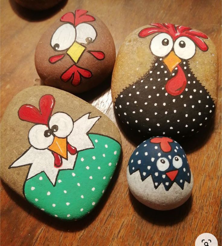 four painted rocks with roosters on them sitting on a wooden table next to each other