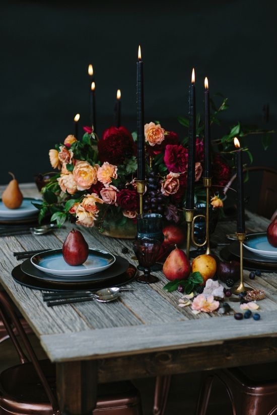 a wooden table topped with plates covered in fruit and flowers next to tall black candles