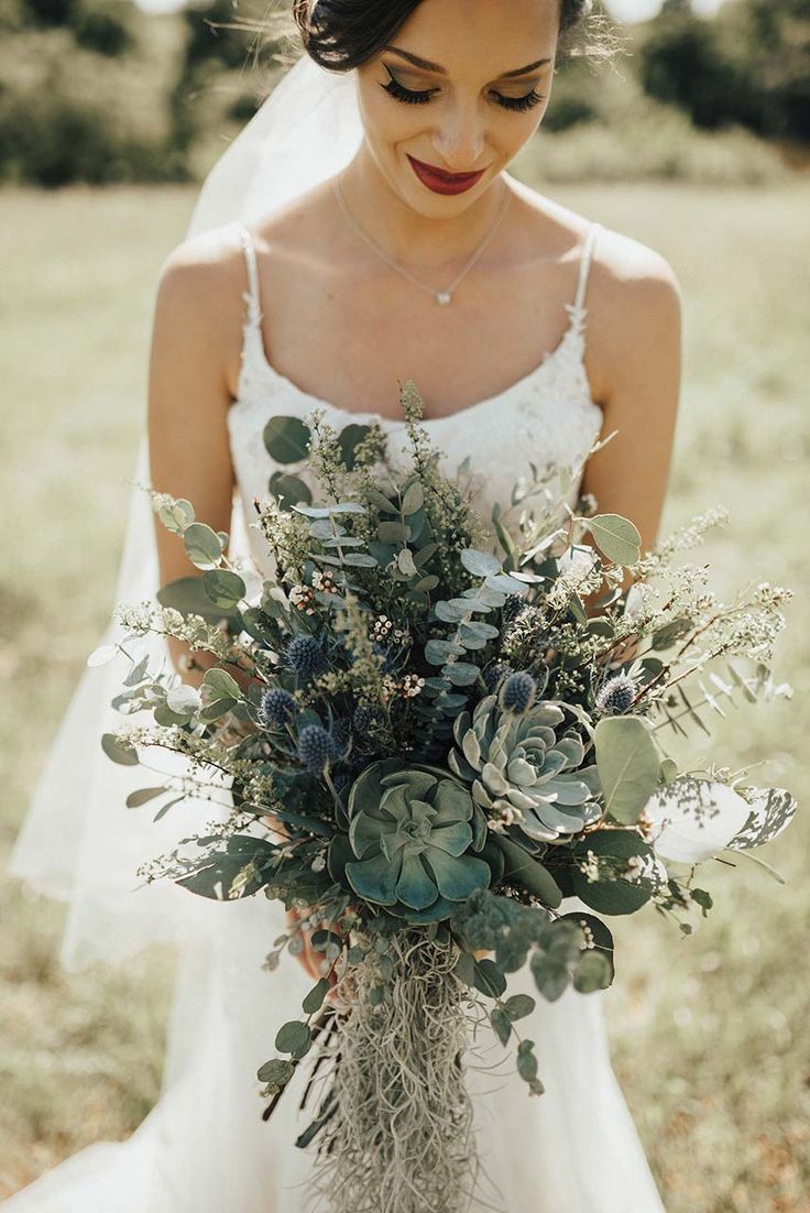 a woman in a wedding dress holding a bouquet with succulents and greenery