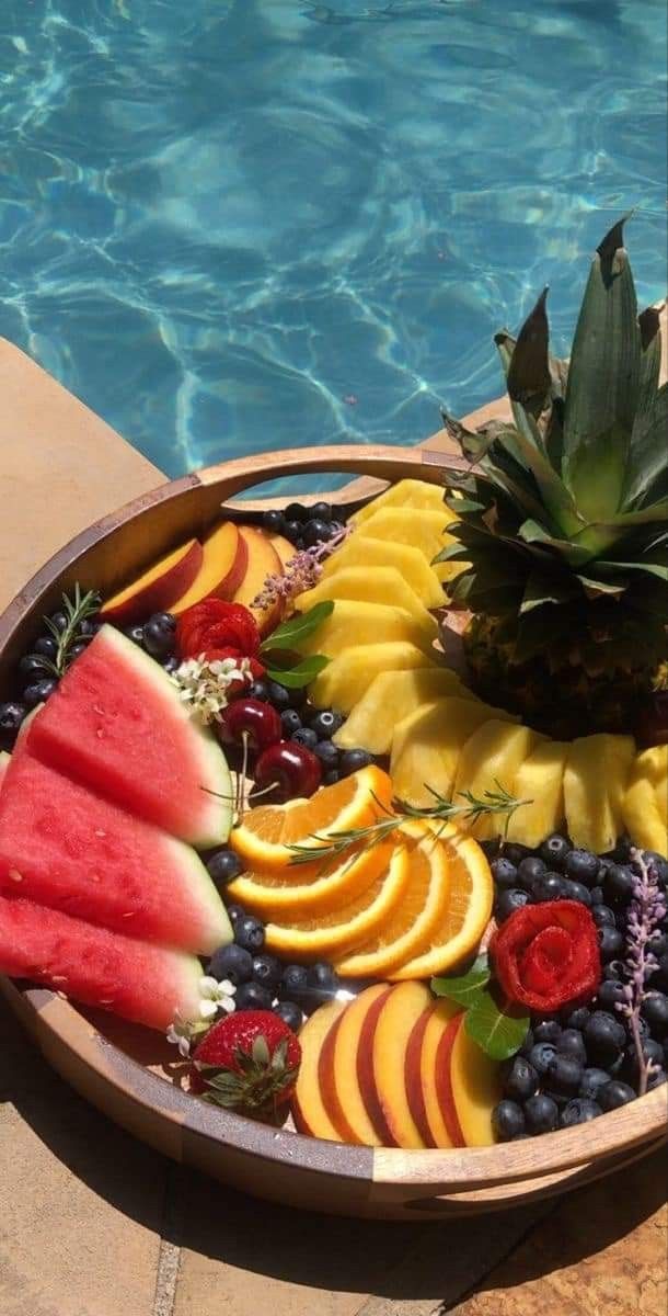 a bowl filled with fruit and watermelon next to a swimming pool in the sun