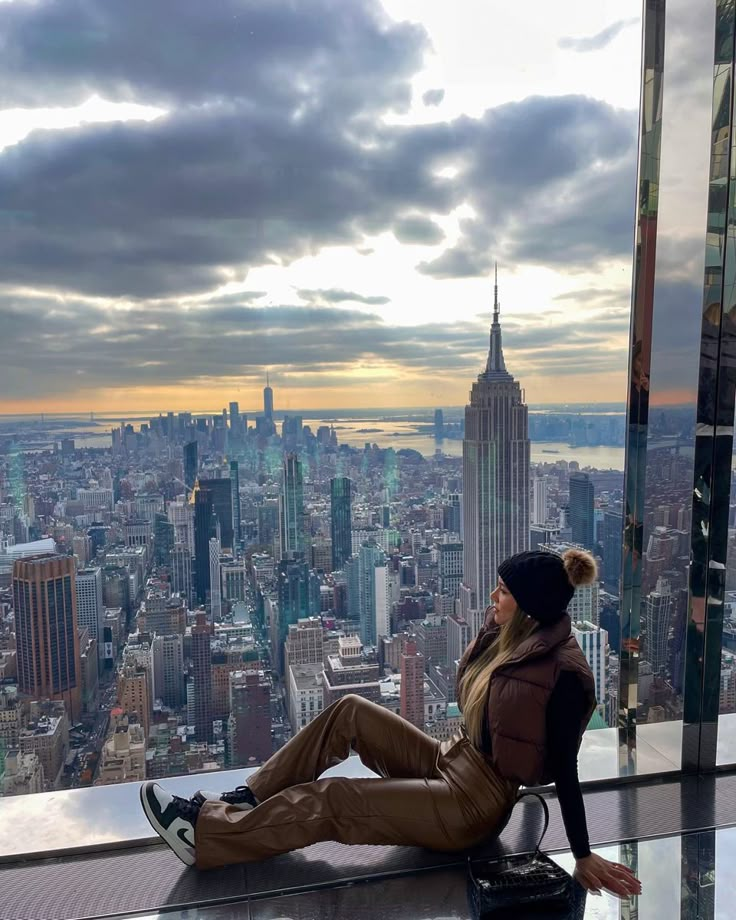 a woman sitting on top of a tall building looking out at the cityscape