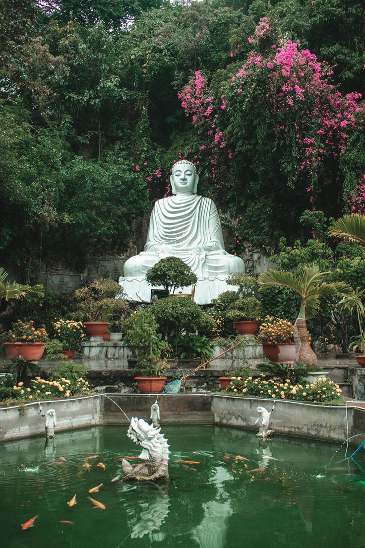 a large white buddha statue sitting in the middle of a pond surrounded by plants and flowers