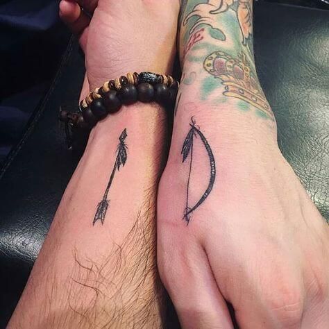 two people with tattoos on their arms holding hands and one has an arrow tattoo on his arm