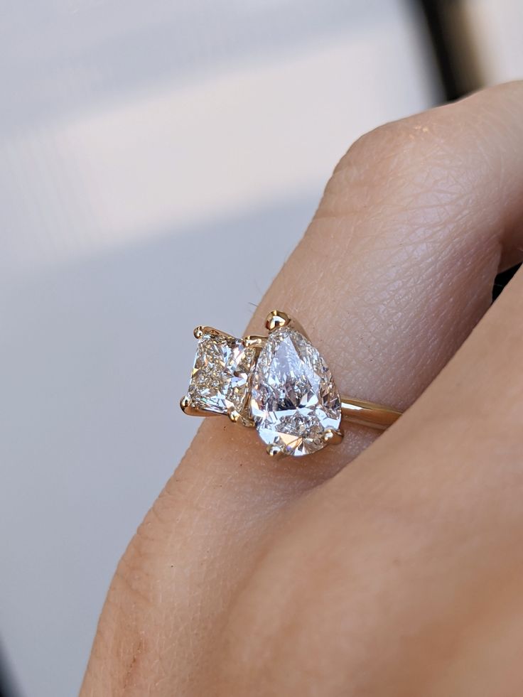 a woman's hand holding a ring with two pear shaped diamonds on top of it