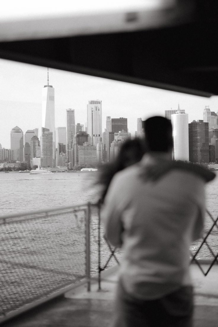 a man and woman are looking out at the water in front of a cityscape