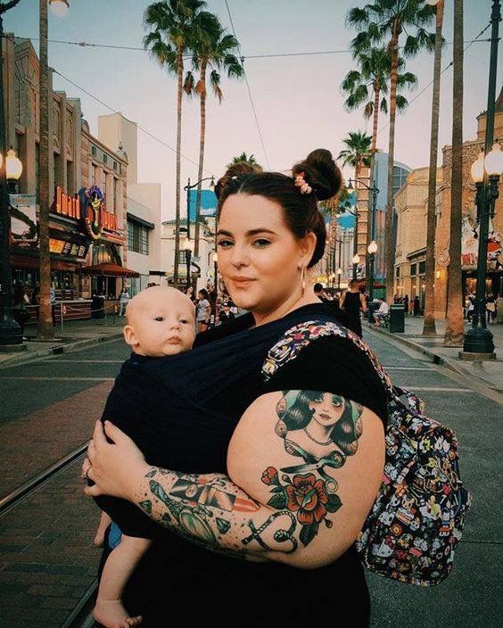 a woman holding a baby in her arms on the street with palm trees behind her