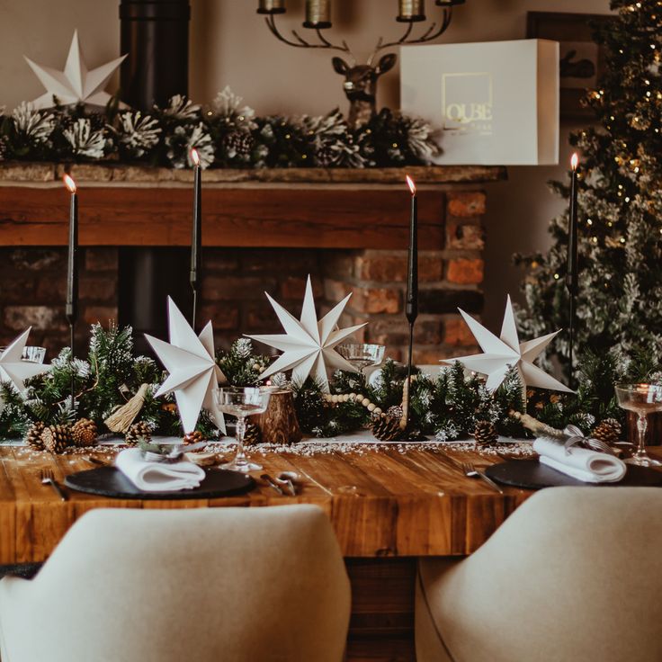 the table is set for christmas dinner with white stars on it and candles in front