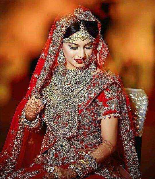 a woman in a red bridal outfit with jewelry on her head and hands behind her back