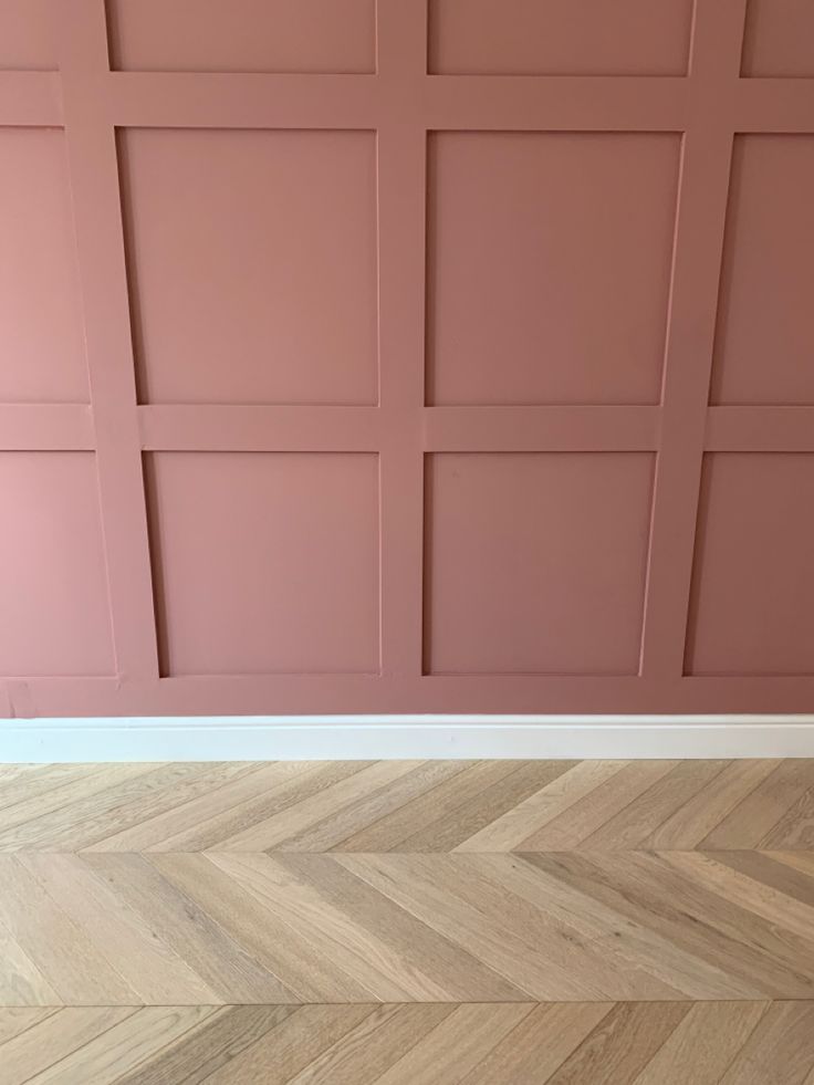 an empty room with pink walls and wood flooring in the foreground is a chevron herringbone pattern