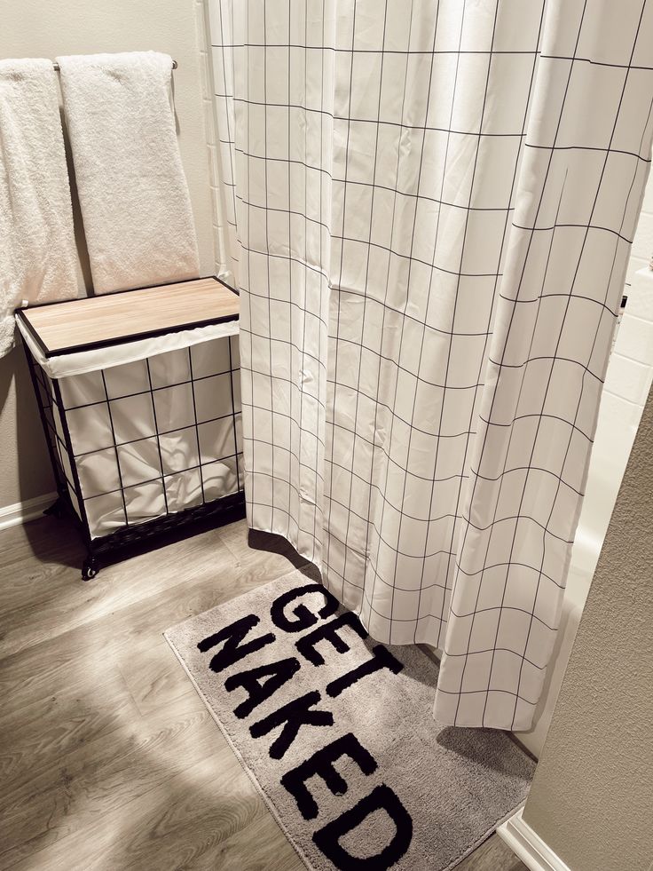 a bathroom with a white shower curtain and a black mat that says make bed on it