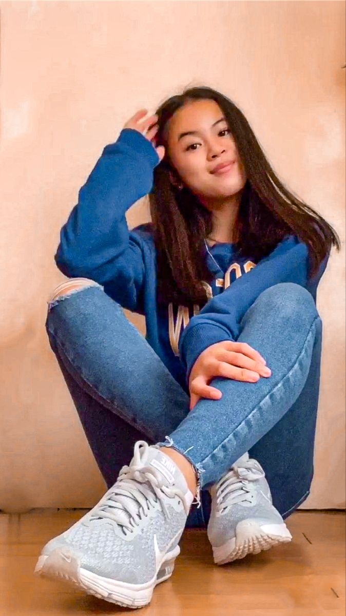 a young woman sitting on the floor with her legs crossed and wearing blue jeans, white sneakers